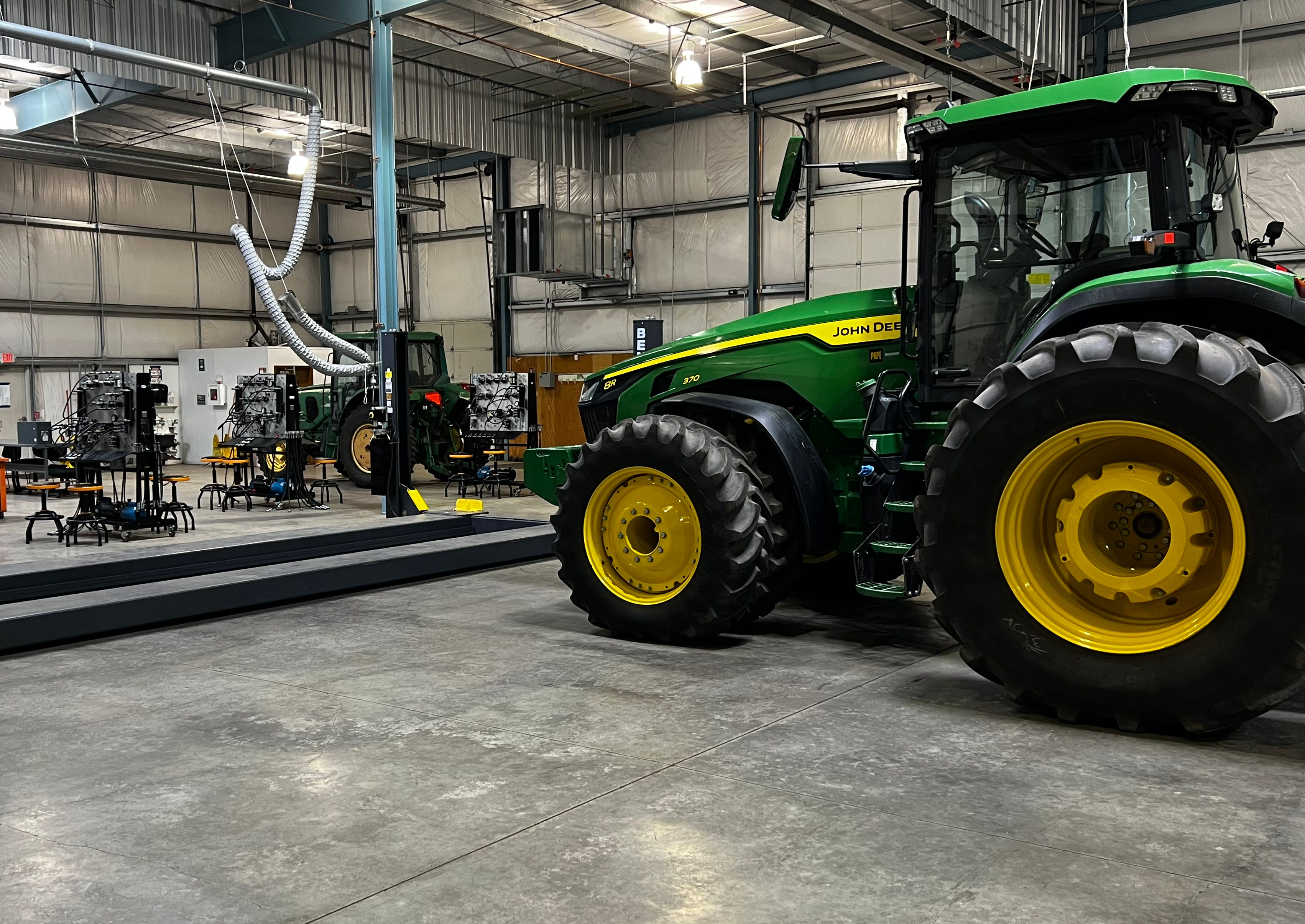 A green John Deere tractor is parked inside the diesel lab. Diagnostics practice stations are visible on the left side.